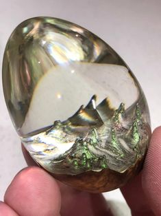 a person holding a large crystal stone in their hand with mountains and trees on it