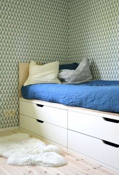 a bedroom with a bed and drawers on the bottom shelf, next to a wallpapered wall