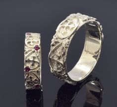 two silver rings sitting on top of a black surface with red stones in the middle