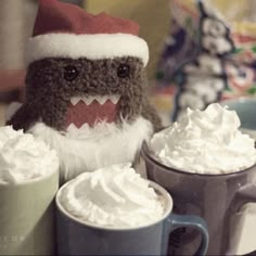 two mugs filled with whipped cream and a stuffed animal wearing a santa claus hat