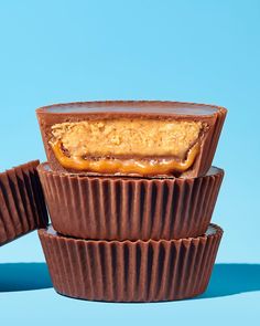 three chocolate cups with peanut butter in them sitting on a blue surface, ready to be eaten