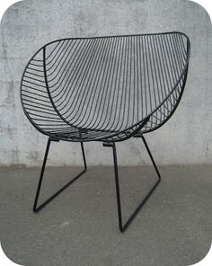 a black wire chair sitting on top of a cement floor next to a concrete wall