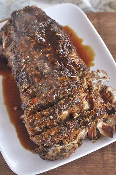 a piece of meat on a plate covered in sauce and gravy, sitting on a wooden table