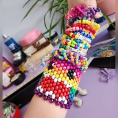 a woman's arm covered in colorful beads and bracelets next to a potted plant