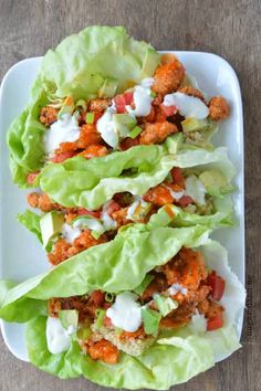 lettuce wraps filled with meat and dressing on a white plate sitting on a wooden table