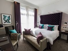 a bed with purple and white pillows in a bedroom next to a desk, chair and lamp