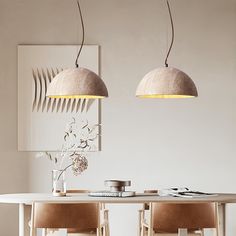 two pendant lights hanging over a dining room table with chairs and vases on it