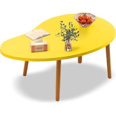 a yellow coffee table with some books and flowers on it, sitting next to a bowl of fruit