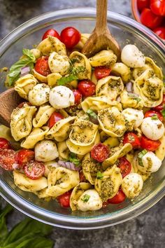 a glass bowl filled with pasta salad and topped with cherry tomatoes, mozzarella cheese and basil