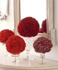 three vases with red flowers in front of a mirror