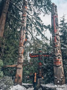 two totem poles standing in the snow near trees