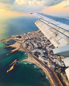 the wing of an airplane flying over a city next to the ocean with buildings on it