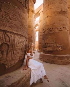 a woman in white dress sitting on the side of an egyptian temple with large columns