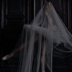 a woman wearing a white dress and veil in front of a black door with her feet on the floor