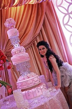 a woman standing next to a large pink cake