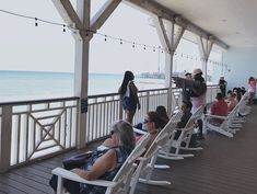 people are sitting on white rocking chairs overlooking the ocean