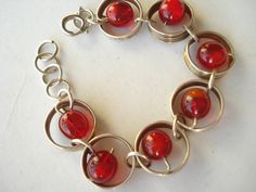 A very pretty, bright bracelet made from silver tone metal swirls with a red glass bead in the centre of each circle.  An unusual design Difficult to date this item so I have described it as 60's. The bracelet has a good  safety clasp and measures almost 7 3/4 inches (19.5 cms) including the clasp..   Please let me know if you need any more information or photos. For more great vintage and Art Deco jewellery go to - http://www.etsy.com/shop/jemimajay?ref=si_shop Vintage Metal Beaded Bracelets, Vintage Round Metal Beaded Bracelets, Red Metal Beaded Bracelet With Round Beads, Vintage Metal Beaded Round Bracelets, Red Metal Costume Jewelry Bracelets, Red Retro Metal Jewelry, Retro Red Metal Jewelry, Retro Red Bracelet Jewelry, Red Metal Costume Jewelry Bracelet