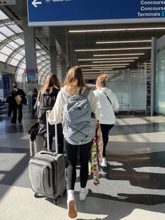 two women walking through an airport with their suitcases and bags on wheels, while another woman is pulling her luggage behind them