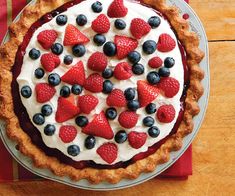 a pie with strawberries, blueberries and raspberries on top sitting on a table