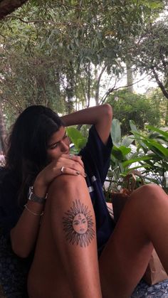 a woman is sitting on the ground with her arm around her neck and sun tattoo