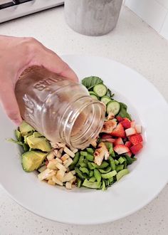 a person pouring dressing onto a salad on a plate with cucumbers and strawberries