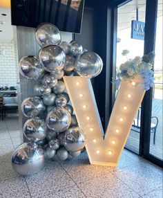 the letter v is made out of silver balloons and lit up with lights in front of it