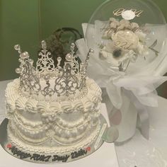 a white wedding cake with a crown on top and flowers in the middle next to it