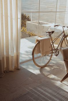 a bicycle parked next to a window in a room with sheer curtains on the windowsill