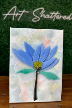 a blue flower on a white card with the words art shattered written in green lettering