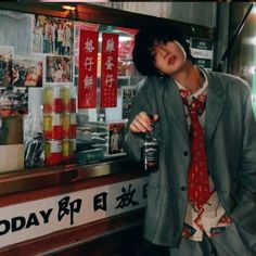 a man standing in front of a food stand holding a bottle and wearing a tie