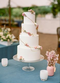 a three tiered white wedding cake with pink flowers on the top and blue table cloth