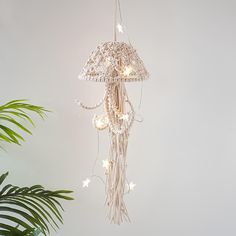 a white chandelier hanging from a ceiling with stars and beads on it, next to a potted plant