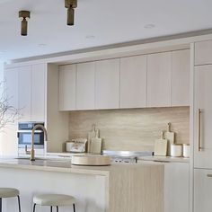 a kitchen with white cabinets and stools next to a counter top that has two vases on it