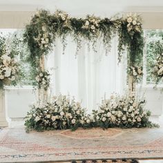 an arrangement of white flowers and greenery on a rug in front of a window