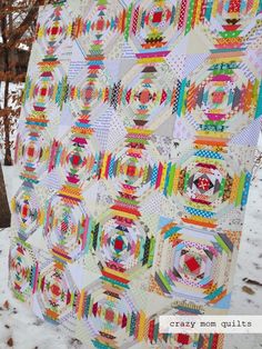 a colorful quilt hanging from the side of a tree in the snow with lots of circles on it