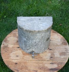 an old stone bucket sitting on top of a wooden table in the grass with green grass behind it