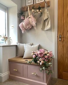 a bench with some flowers on it in front of a wall mounted coat rack and window