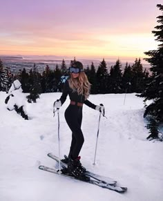 a woman riding skis down the side of a snow covered slope with trees in the background