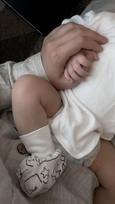 a baby laying on top of a bed next to a person's hand holding it