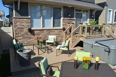 an outdoor deck with hot tub, chairs and table in front of the house on a sunny day