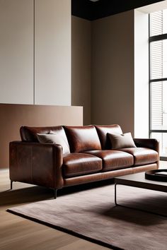 a brown leather couch sitting on top of a wooden floor next to a large window