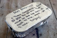 a piece of cake with writing on it sitting on top of a wooden table and covered in tin foil