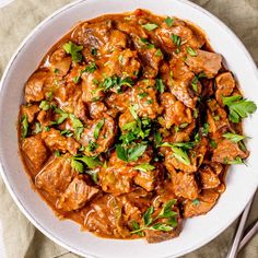 a white bowl filled with meat covered in sauce and garnished with parsley