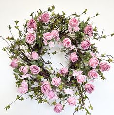 a wreath with pink roses and greenery on it is displayed against a white wall