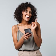 a woman smiling and holding a cell phone in one hand and pointing to the other