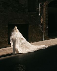 a woman in a wedding dress is walking down the street with her veil draped over her head