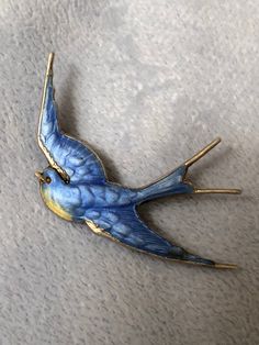 a blue bird brooch sitting on top of a white cloth covered floor next to a wall