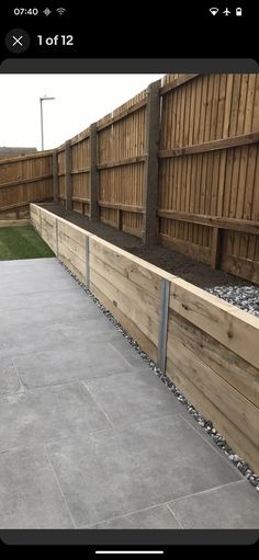 a wooden fence next to a grass covered yard with gravel on the ground and rocks in the middle