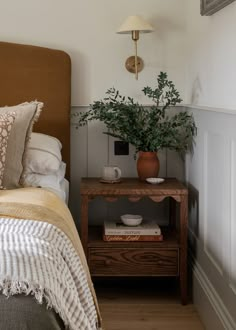 a bed room with a neatly made bed and a plant on the nightstand next to it