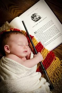 a baby wrapped in a blanket and holding a wand next to an open harry potter book